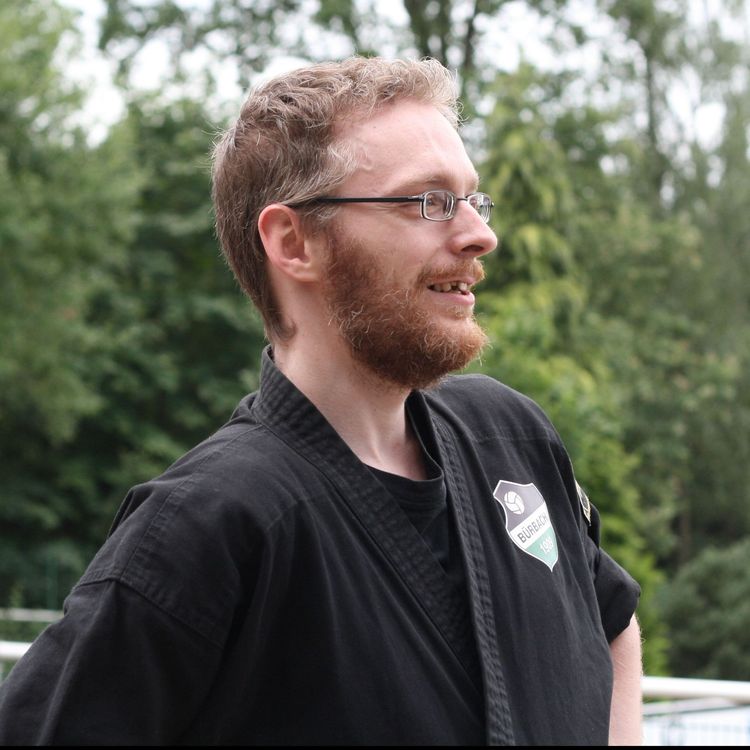 Ein Bild von Jens Uwe Becker vor einem grünen Buschwerk. Das Bild zeigt ihn von der rechten Seite.