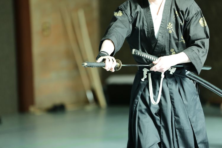 Person in a black martial arts suite with two swords in the belt is drawing his katana