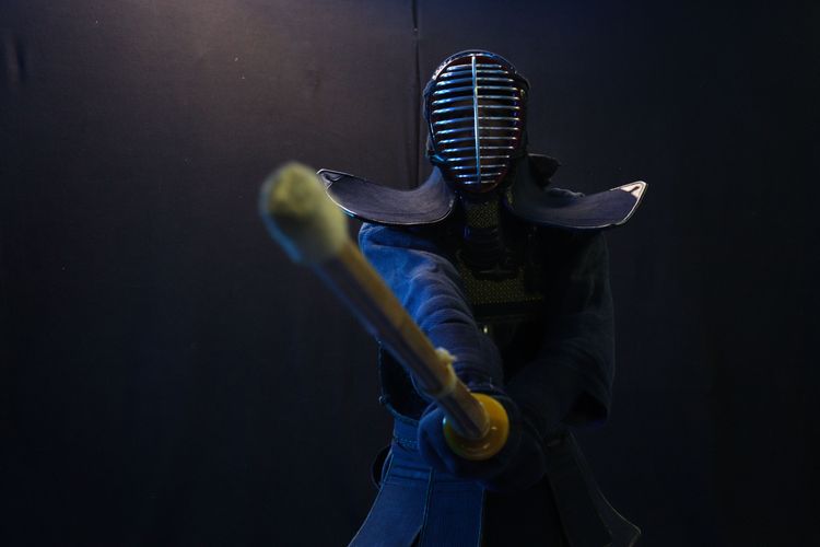 A kendo-ka in full armor is pointing his shinai directly into the camery